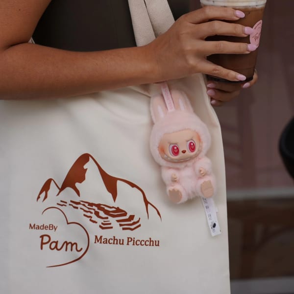 A person holding a chocolate drink with whipped cream, carrying a tote bag with a pink bunny charm.
