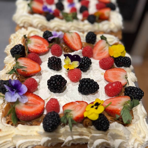 Close-up of a layered dessert with whipped cream, strawberries, raspberries, blackberries, and edible flowers.