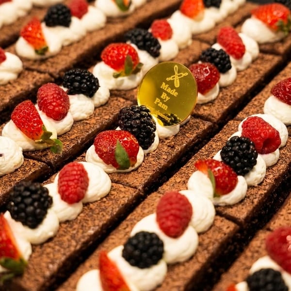 Rows of chocolate brownies topped with whipped cream, strawberries, raspberries, and blackberries.