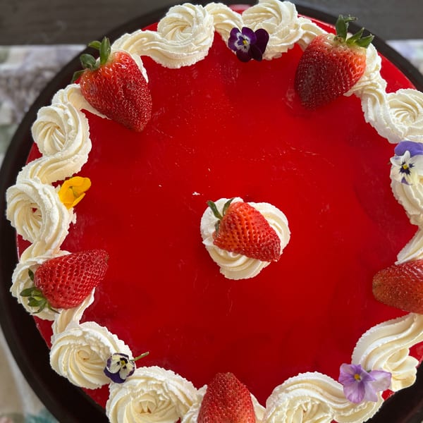 Overhead view of a vibrant red strawberry cake with whipped cream swirls and edible flowers.