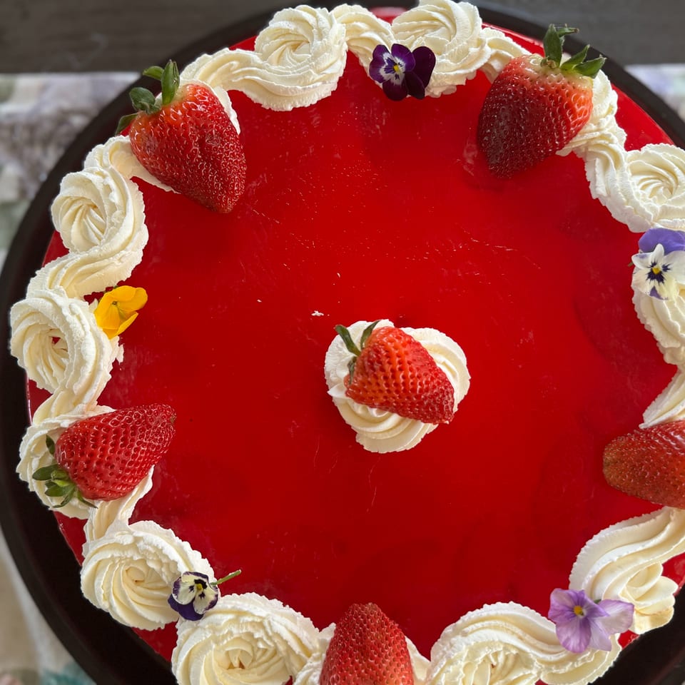 Overhead view of a vibrant red strawberry cake with whipped cream swirls and edible flowers.