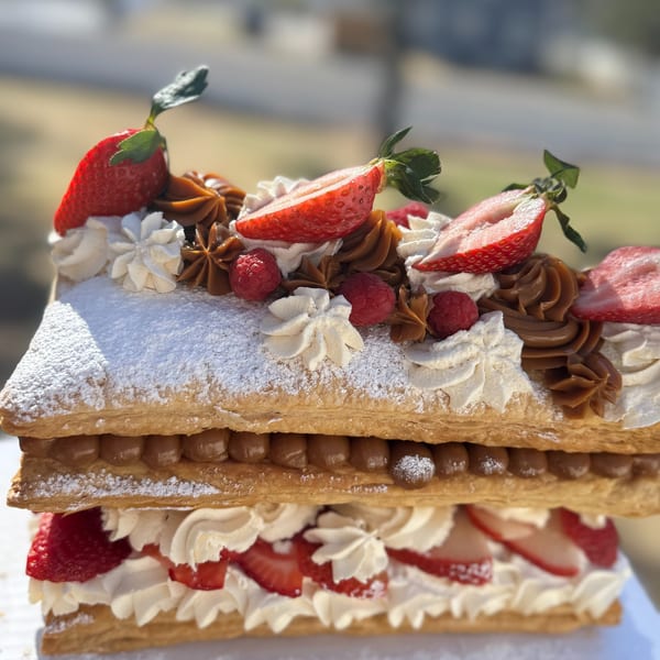 A multi-layered pastry with dulce de leche, whipped cream, strawberries, and raspberries, dusted with powdered sugar.