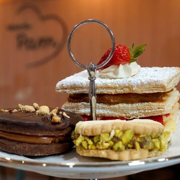 A tiered dessert stand holds a chocolate alfajor, pistachio cookie, and a strawberry mille-feuille.