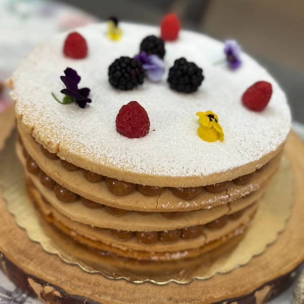 A layered cake with dulce de leche filling, powdered sugar, raspberries, blackberries, and edible flowers.