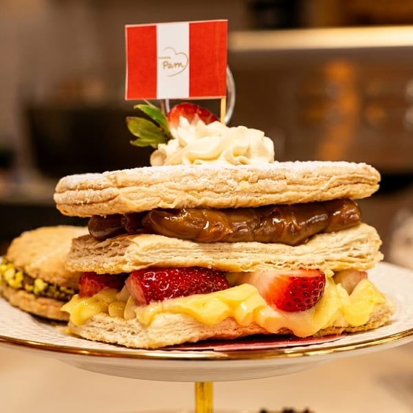 A Peruvian flag tops a layered pastry with dulce de leche, strawberries, and cream on a white plate.