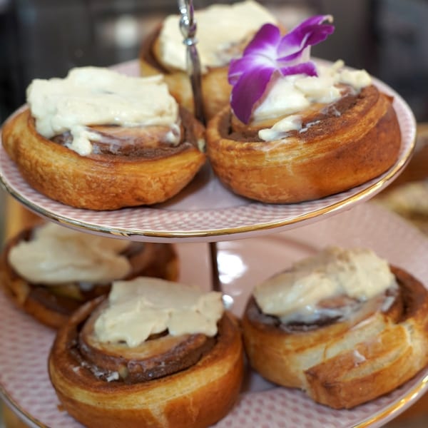 Tiered stand with cinnamon rolls topped with cream cheese frosting, one garnished with a purple orchid.