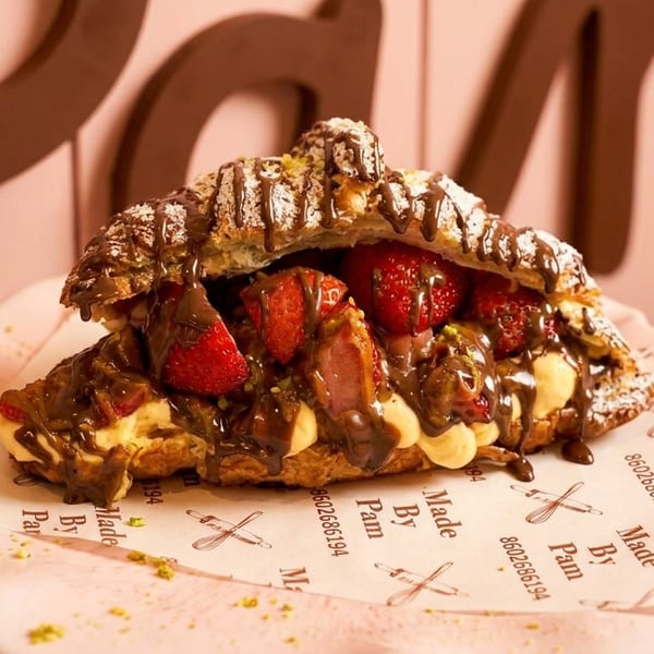 A croissant filled with strawberries, cream, and chocolate drizzle, on a pink plate.