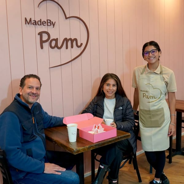 Three people, two customers and one staff member, smiling in the "MadeBy Pam" bakery.
