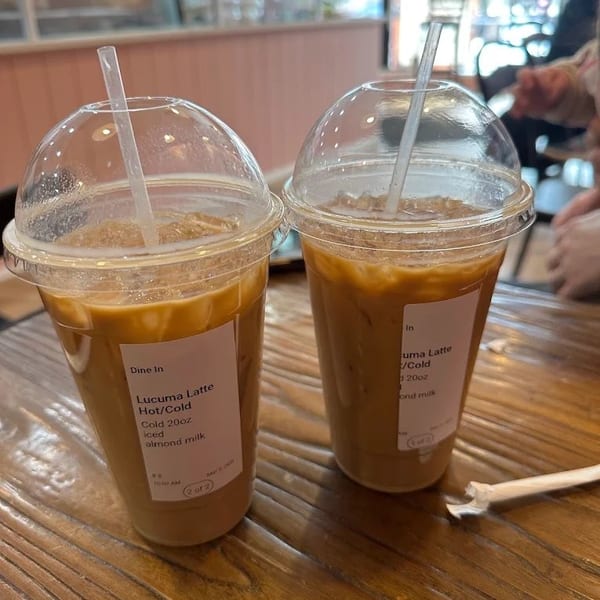 Two iced lucuma lattes with almond milk in plastic cups on a wooden table.