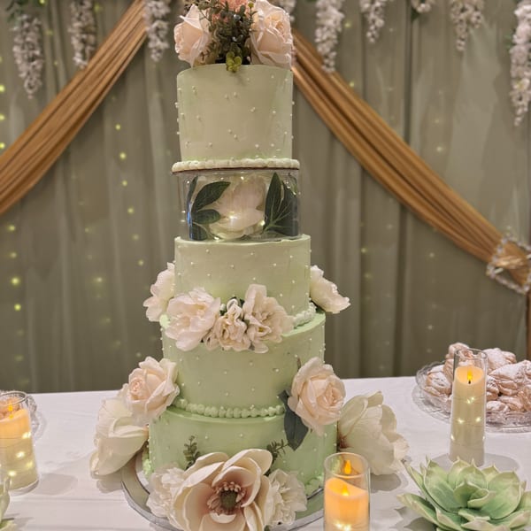 A five-tier light green cake with white floral decorations and a "Mis 15" topper.